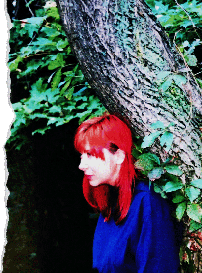 Photo de l'artiste peintre Patricia Huber, pensive dans la nature, accotée sur un tronc d'arbre.